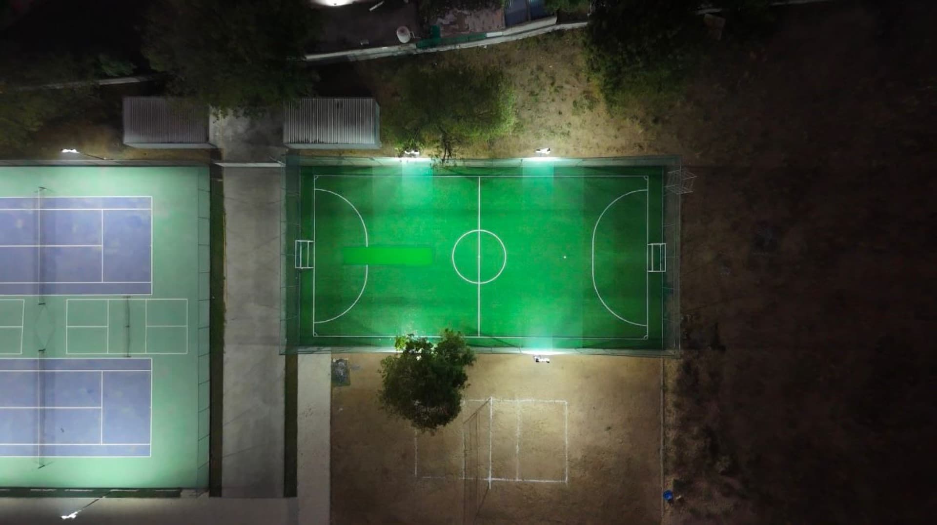 Drona Sports Academy's floodlit tennis courts and turf ground at night